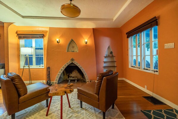 A room with a fireplace, leather chairs, a wooden table, and a large window. - Sam Hughes Retreat by Velo (Tucson)