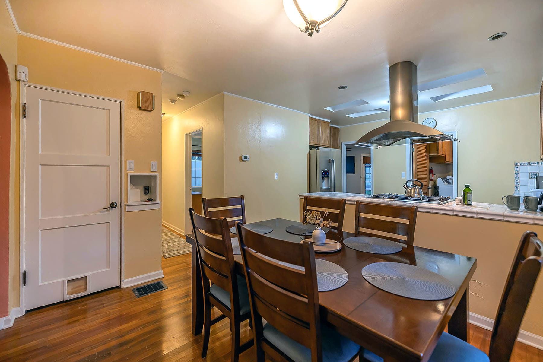 A dining area with a wooden table and chairs, a kitchen with a stove and cabinets, and a door leading to another room.