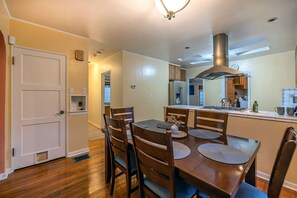 A dining area with a wooden table and chairs, a kitchen with a stove and cabinets, and a door leading to another room. - Sam Hughes Retreat by Velo (Tucson)