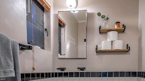 A bathroom with a sink, toilet, and mirror. There is a towel rack and a shelf with toiletries.
