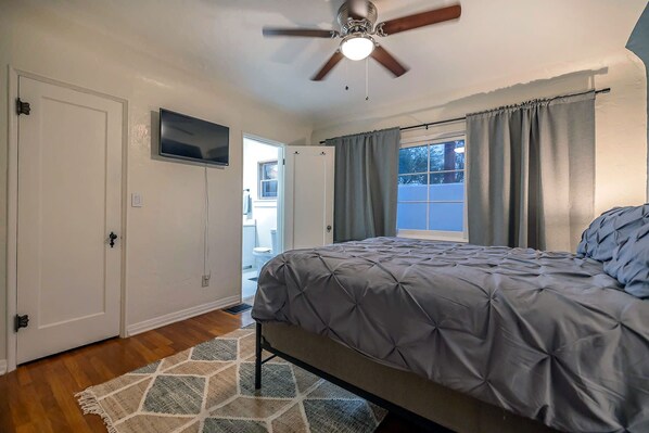Un dormitorio con cama, ventilador de techo, televisor y ventana con cortinas.