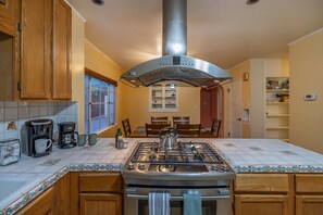 Una cocina con estufa a gas, armarios de madera, una ventana y un comedor con sillas y mesa.