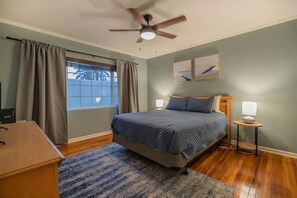 A bedroom with a bed, two bedside lamps, a ceiling fan, a window with curtains, and a desk. - Sam Hughes Retreat by Velo (Tucson)