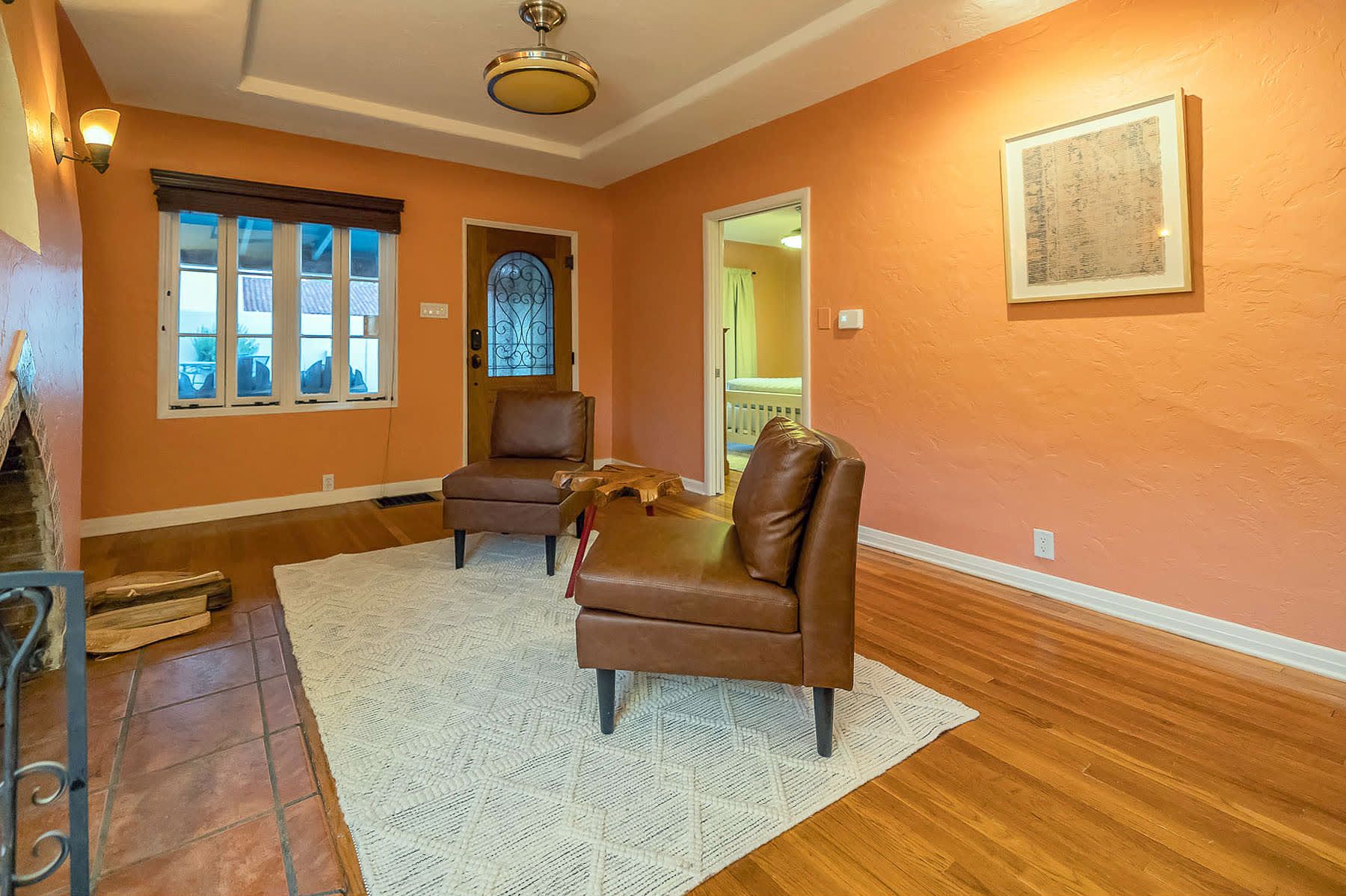 A room with two brown leather chairs, a white rug, wooden flooring, a window with blinds, a door with a decorative glass panel, and a ceiling fan.