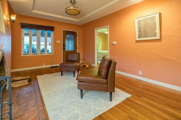 A room with two brown leather chairs, a white rug, wooden flooring, a window with blinds, a door with a decorative glass panel, and a ceiling fan. - Sam Hughes Retreat by Velo (Tucson)