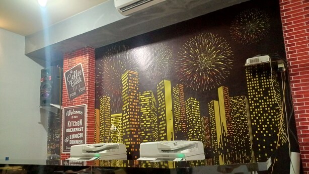 A restaurant with a cityscape mural, a coffee machine, and a sign welcoming guests to the kitchen breakfast and lunch diner. - OYO 93090 Multi Plus Inn (Jayapura)