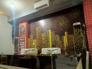 A restaurant with a cityscape mural, a coffee machine, and a sign welcoming guests to the kitchen breakfast and lunch diner. - OYO 93090 Multi Plus Inn (Jayapura)