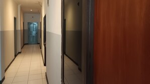 A corridor with a tiled floor, a wooden door, and a blue door in the distance. - OYO 93090 Multi Plus Inn (Jayapura)