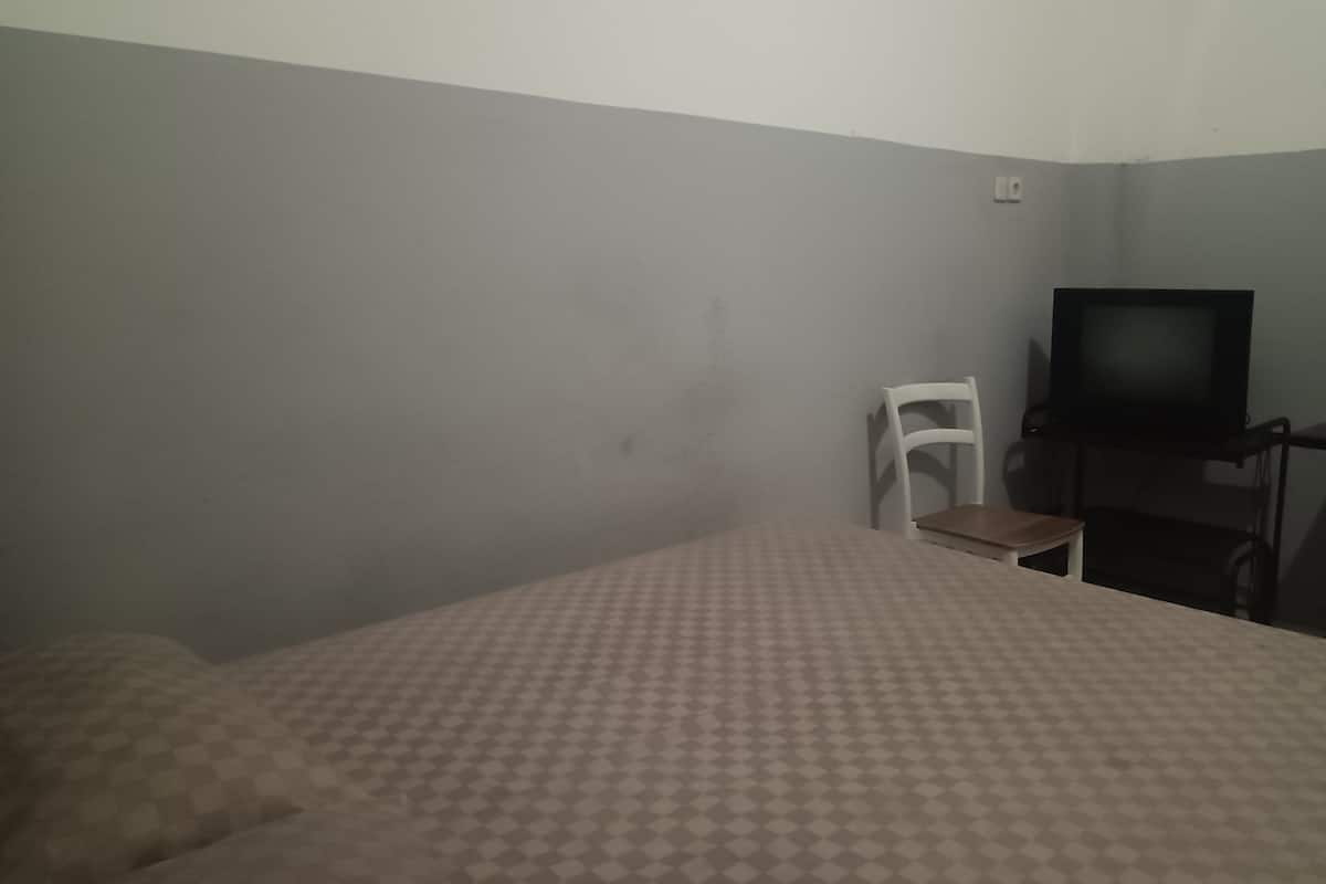 A room with a bed, a television, and a white chair.