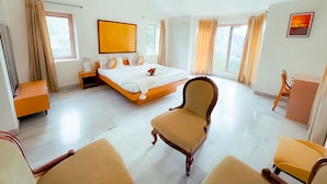 A spacious hotel room with a large bed, two chairs, a desk, and a ceiling fan. - Roomshala 131 Willow Woods Farmhouse (Sohna)
