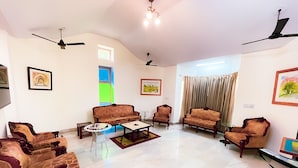 A spacious living room with a high ceiling, multiple ceiling fans, and a variety of seating options including sofas and armchairs. - Roomshala 131 Willow Woods Farmhouse (Sohna)