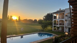 A swimming pool with a view of a sunset, a grassy area, and a multi-story building with balconies. - Ideal apartment for golf lovers or families, with communal pool in Mijas Golf! (Mijas costa)
