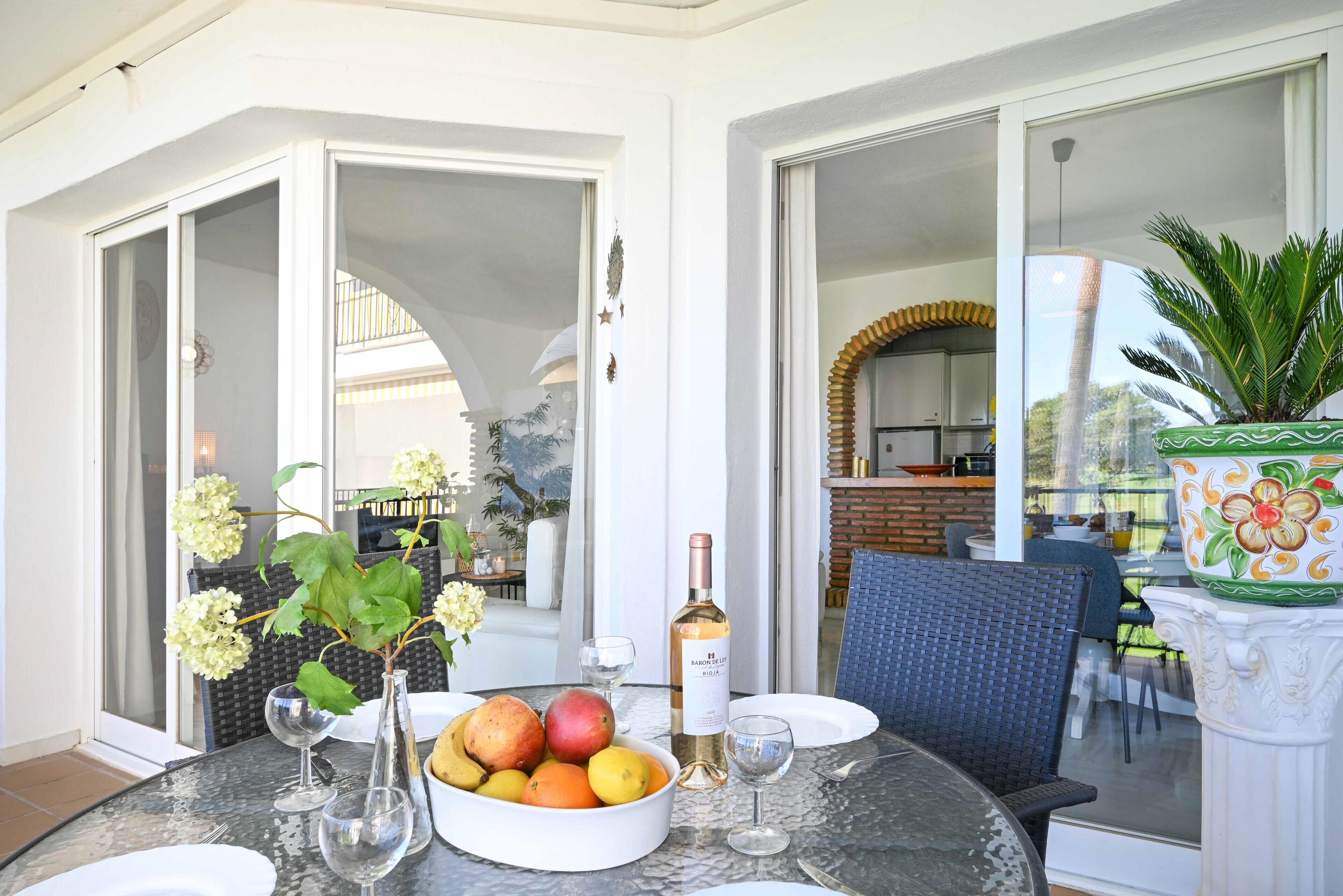Une table à manger avec un panier de fruits, des verres à vin et une bouteille de vin.