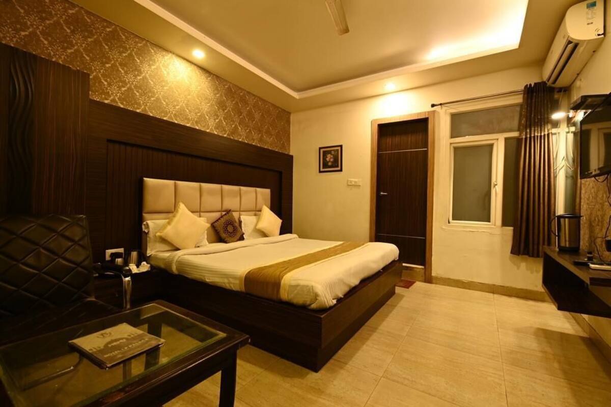 A hotel room with a large bed, a glass coffee table, a dark wooden headboard, and a built-in air conditioning unit.
