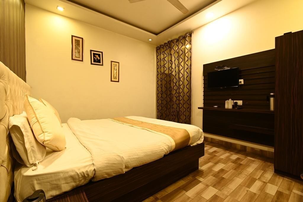 A bedroom with a bed, a TV on a wooden shelf, and framed pictures on the wall.