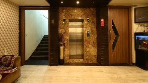 A modern lobby with a marble wall, an elevator, a staircase, a sofa, and a television. - Hotel I.P. Palace (Lucknow)