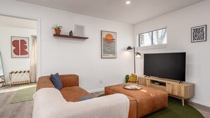 Una sala de estar moderna con un sofá marrón, una mesa de centro y un televisor de pantalla plana. Se observan estantes empotrados con objetos decorativos y un cuadro enmarcado.