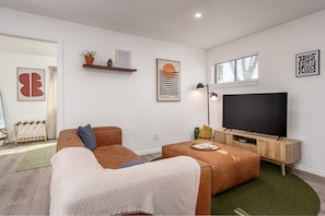 Una sala de estar moderna con un sofá marrón, una mesa de centro y un televisor de pantalla plana. Se observan estantes empotrados con objetos decorativos y un cuadro enmarcado.