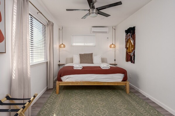 Un dormitorio con cama, ventilador de techo, ventana con persianas y aire acondicionado de pared.