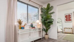 Una habitación con una consola blanca, una planta grande en maceta, un espejo y un perchero de madera.