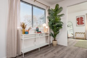 Una habitación con una consola blanca, una planta grande en maceta, un espejo y un perchero de madera.