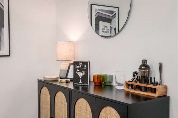 Un espace bar comprenant un livre de recettes de cocktails, une lampe et les ustensiles nécessaires à la préparation des cocktails.