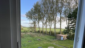 A view through a window of a grassy yard with a wooden table and a shed. - Ecolodge Loft, 180qm Raumwunder für bis zu 8 Personen, 5km zu Nordsee / Büsum (Oesterdeichstrich)