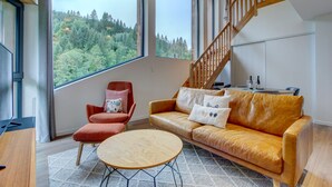 A modern living room with a wooden staircase, a red armchair, a leather sofa, and a round coffee table. - Alptitude Beauvallon Petit - stylish and spacious property for 6 people (Morzine)