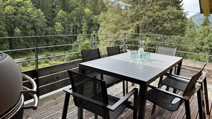 An outdoor deck with a table and chairs, overlooking a forested area. - Alptitude Beauvallon Petit - stylish and spacious property for 6 people (Morzine)