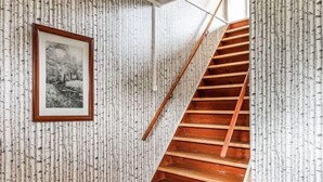 Un escalier en bois avec une rampe, une photographie en noir et blanc encadrée accrochée au mur, et un papier peint texturé avec des motifs de lignes verticales.