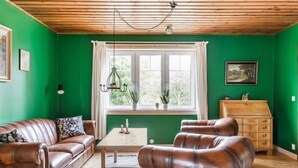 Une pièce aux murs verts, avec un plafond en bois, des canapés en cuir, une table en bois, une commode et une fenêtre avec des rideaux.