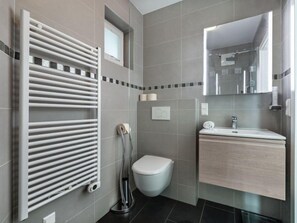 A modern bathroom with a white toilet, a glass shower enclosure, a white sink, and a towel rack.