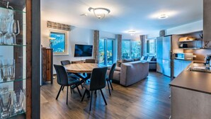 A modern kitchen with a dining area, large windows, and a flat-screen TV.