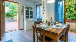 Comedor con mesa de madera dispuesta para cuatro, un armario blanco con puertas de cristal y vistas al exterior.
