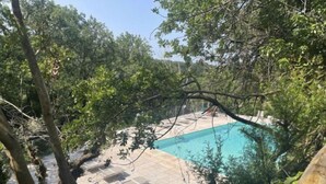 Una piscina rodeada de árboles, con un área de terrazas con baldosas.