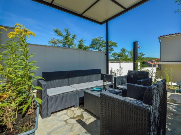 An outdoor patio with a sofa and chairs, a small table, and a potted plant.