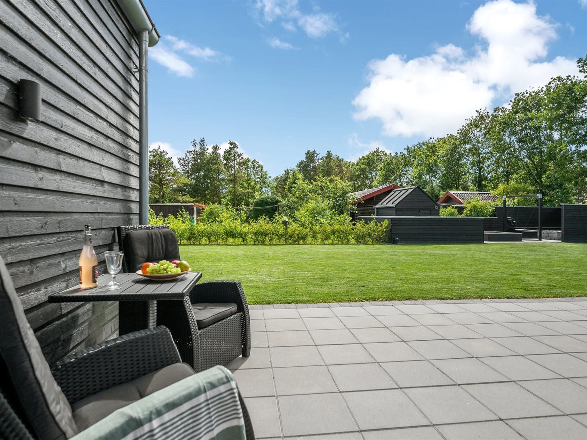 Une terrasse extérieure avec une table dressée pour deux personnes, une bouteille de vin et une assiette de fruits.