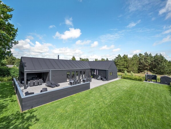Ett modernt hus med en täckt uteplats, en gräsmatta och en skogsliknande bakgrund.