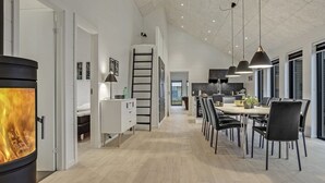 Une cuisine moderne dotée d’un îlot central, d’un coin repas avec une longue table et d’une cheminée visible.