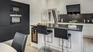 Une cuisine moderne avec des meubles de rangement noirs, un îlot central doté de tabourets de bar, un four encastré et un téléviseur à écran plat fixé au-dessus de l’îlot.