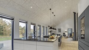 Une cuisine moderne dotée d’un grand îlot central, de luminaires suspendus et offrant une vue sur l’extérieur.