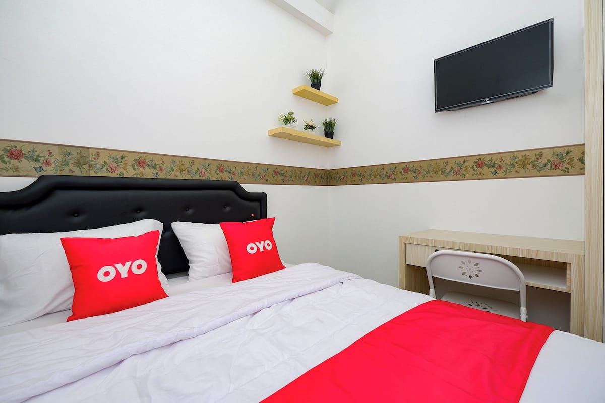 A hotel room with a bed, a desk, a TV, and two wall-mounted shelves with plants.
