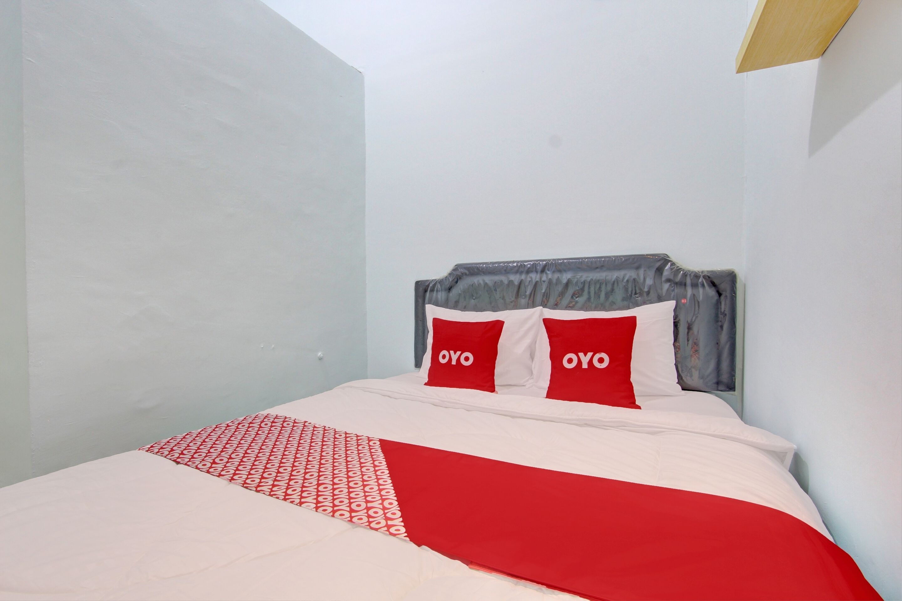 A bed with a white and red bedspread, two pillows with the word "OYO" on them, and a grey headboard.