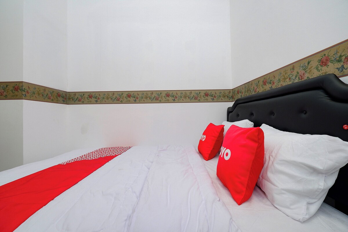 A hotel room with a bed, red and white pillows, and a floral border on the wall.
