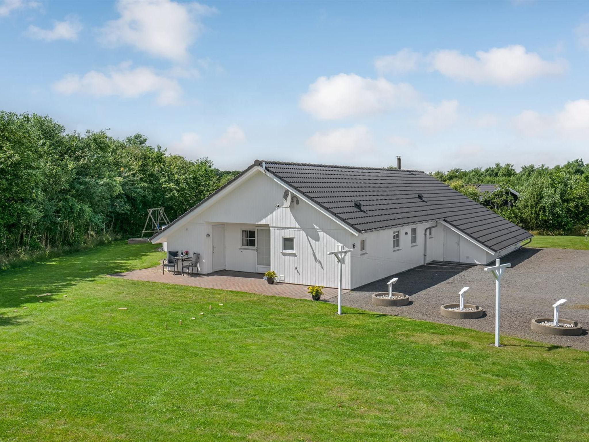 Ein eingeschossiges weißes Haus mit geneigtem Dach, einer Terrasse mit Gartenmöbeln und einem gepflegten Rasen.
