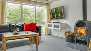 A modern living room with a black leather sofa, a wooden coffee table, a TV mounted on the wall, and a wood-burning stove.