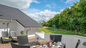 A patio with a table set for breakfast, outdoor chairs, and a view of a grassy area with trees.