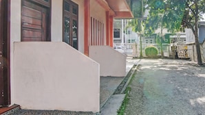 Ein Gebäude mit befestigtem Eingangsbereich, einem kleinen Garten und einem weißen Zaun.