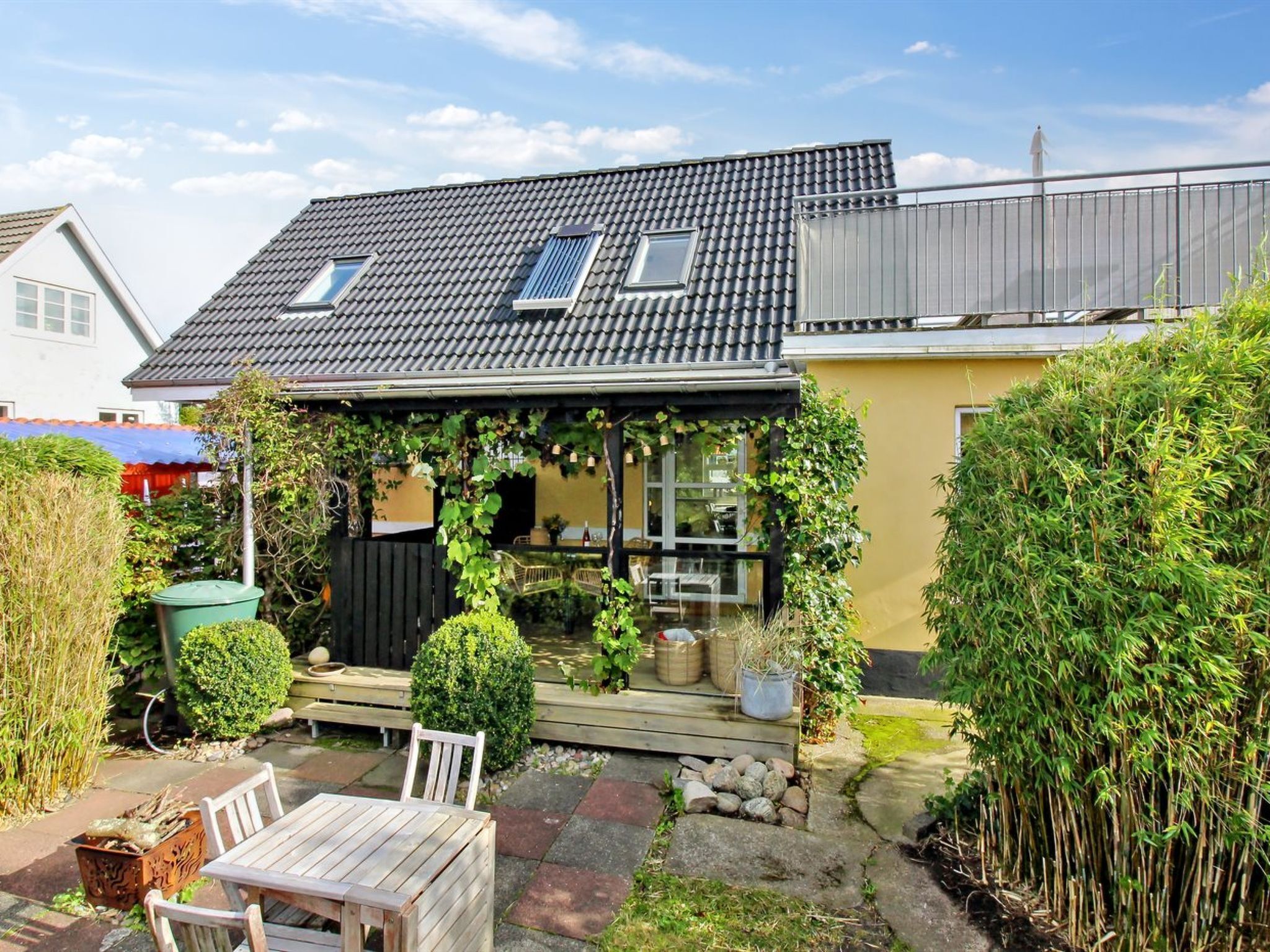 Ein Wohnhaus mit Ziegeldach, einer Veranda und einem Garten mit Holztisch und Stühlen.