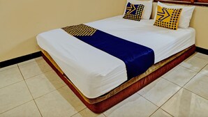 Una cama con ropa de cama blanca y azul, dos almohadas con diseños amarillos y negros, y un cabecero de madera.